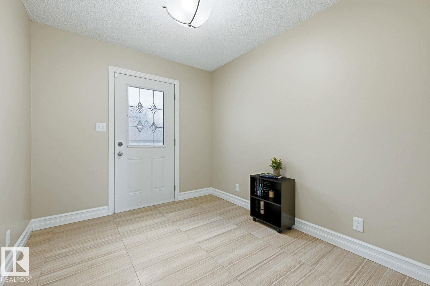 Entryway featuring a white door with decorative glass, light-colored tile flooring, and a flush-mount ceiling light - 11317 22 Avenue Nw, Edmonton, AB