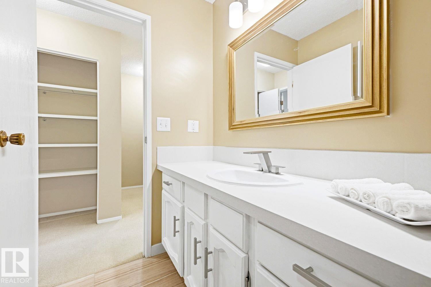 Vanity featuring an integrated sink, polished chrome faucet, white cabinetry with silver-tone hardware, and a framed mirror - 11317 22 Avenue Nw, Edmonton, AB