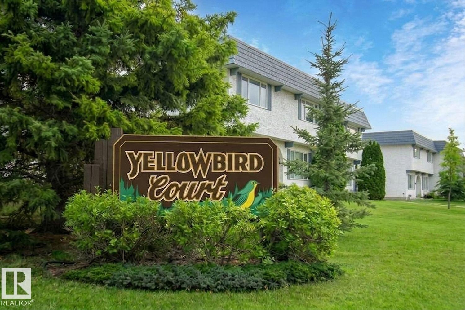 Stucco-sided building with dark shingled mansard roofs, surrounded by mature evergreen trees - 11317 22 Avenue Nw, Edmonton, AB