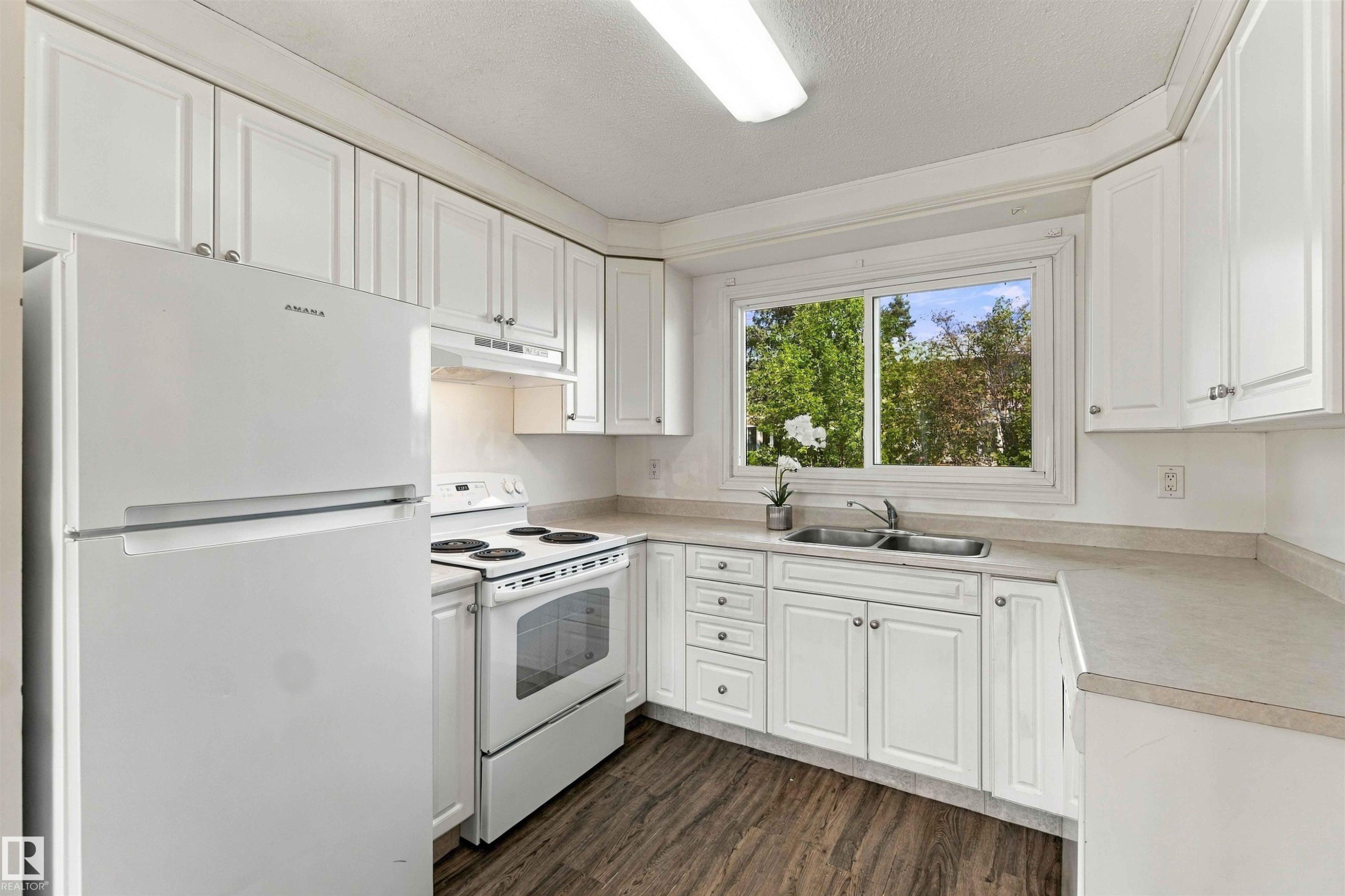 Kitchen featuring white cabinetry, wood-finish flooring, a double basin sink, and a large window - 17351 85 Avenue Nw, Edmonton, AB