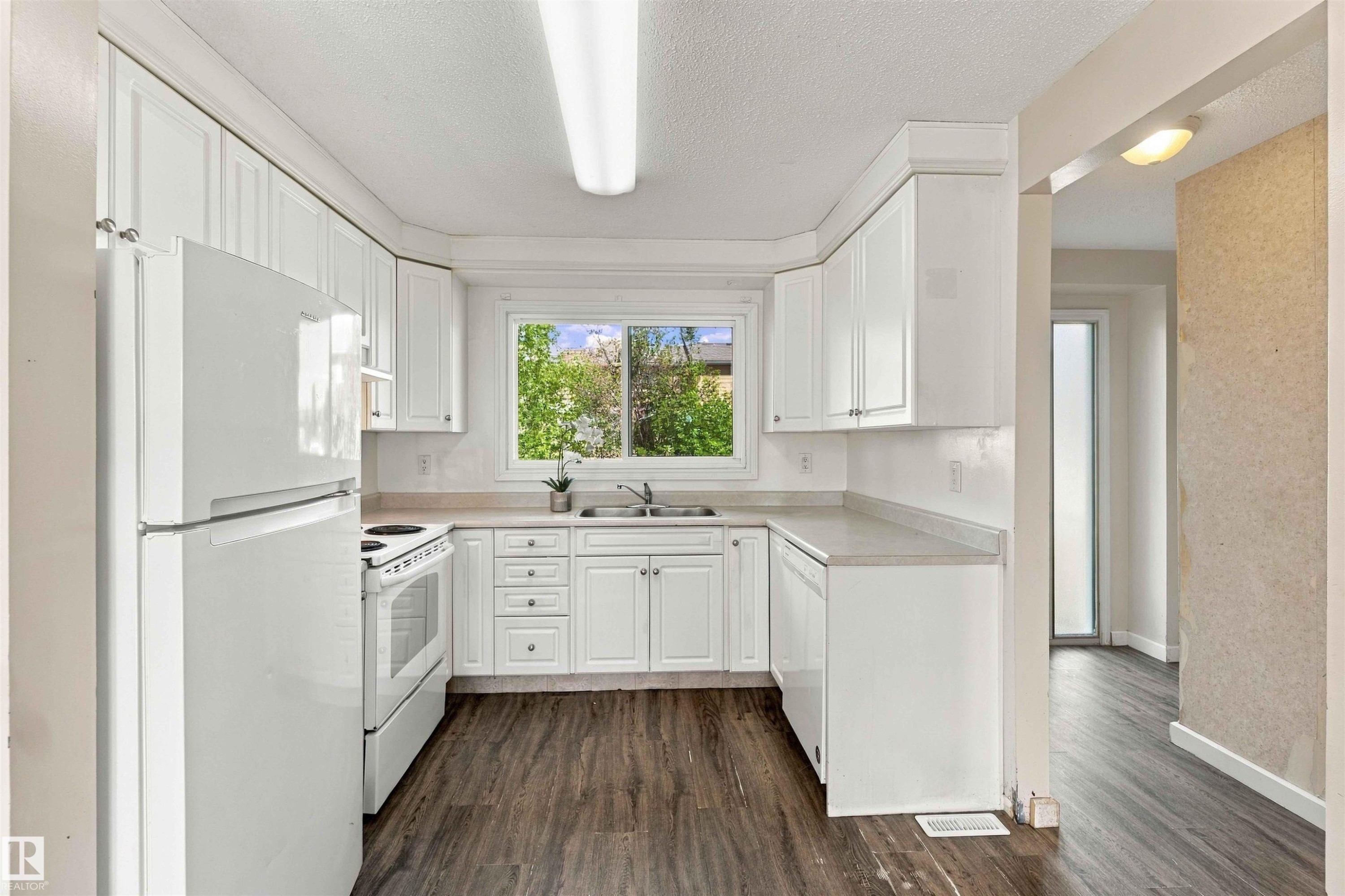 U-shaped kitchen with white cabinetry, wood-finish flooring, and a double basin sink - 17351 85 Avenue Nw, Edmonton, AB
