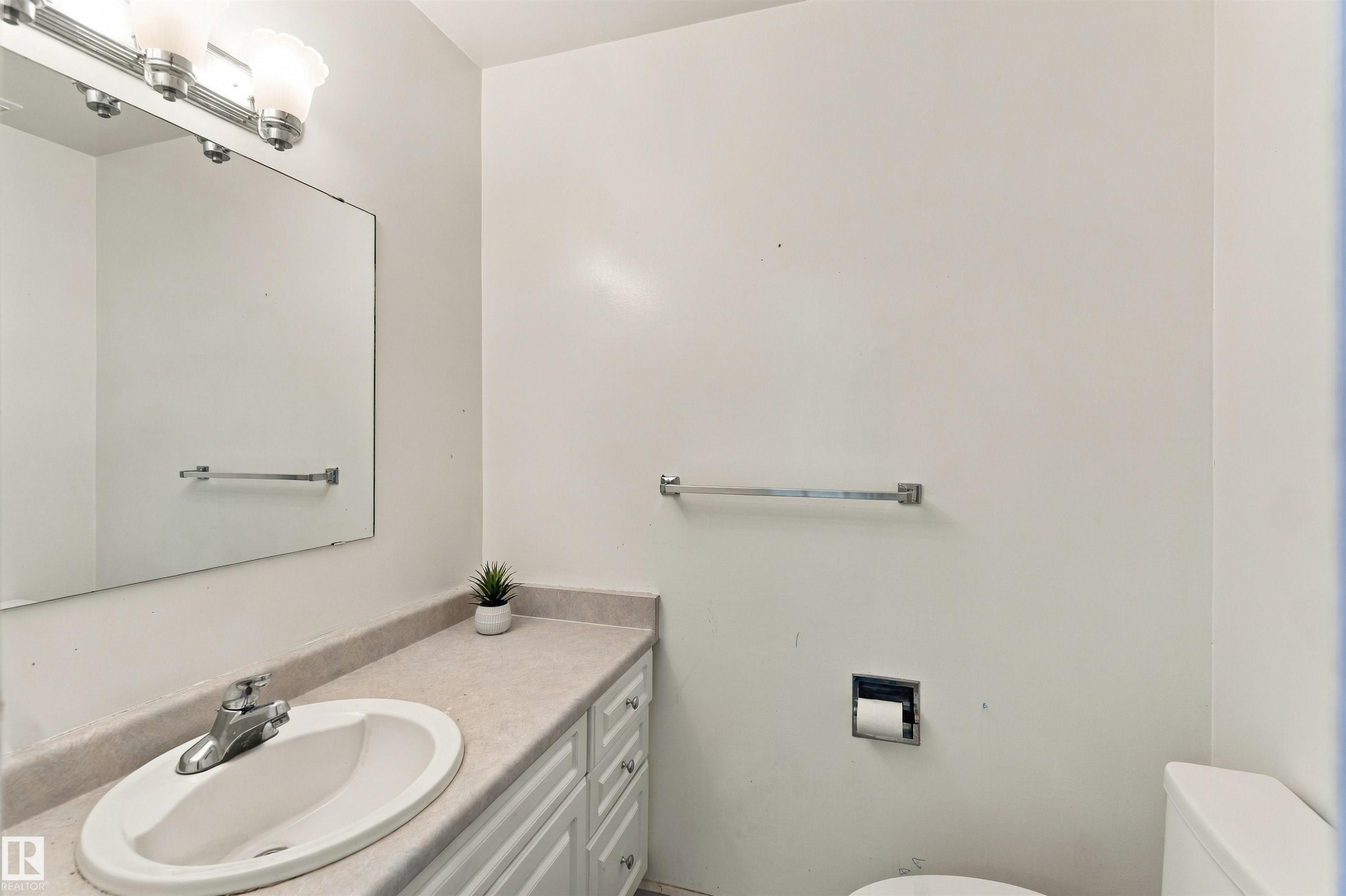 Bathroom featuring a vanity with an integrated sink, a rectangular mirror, and a three-light fixture - 17351 85 Avenue Nw, Edmonton, AB
