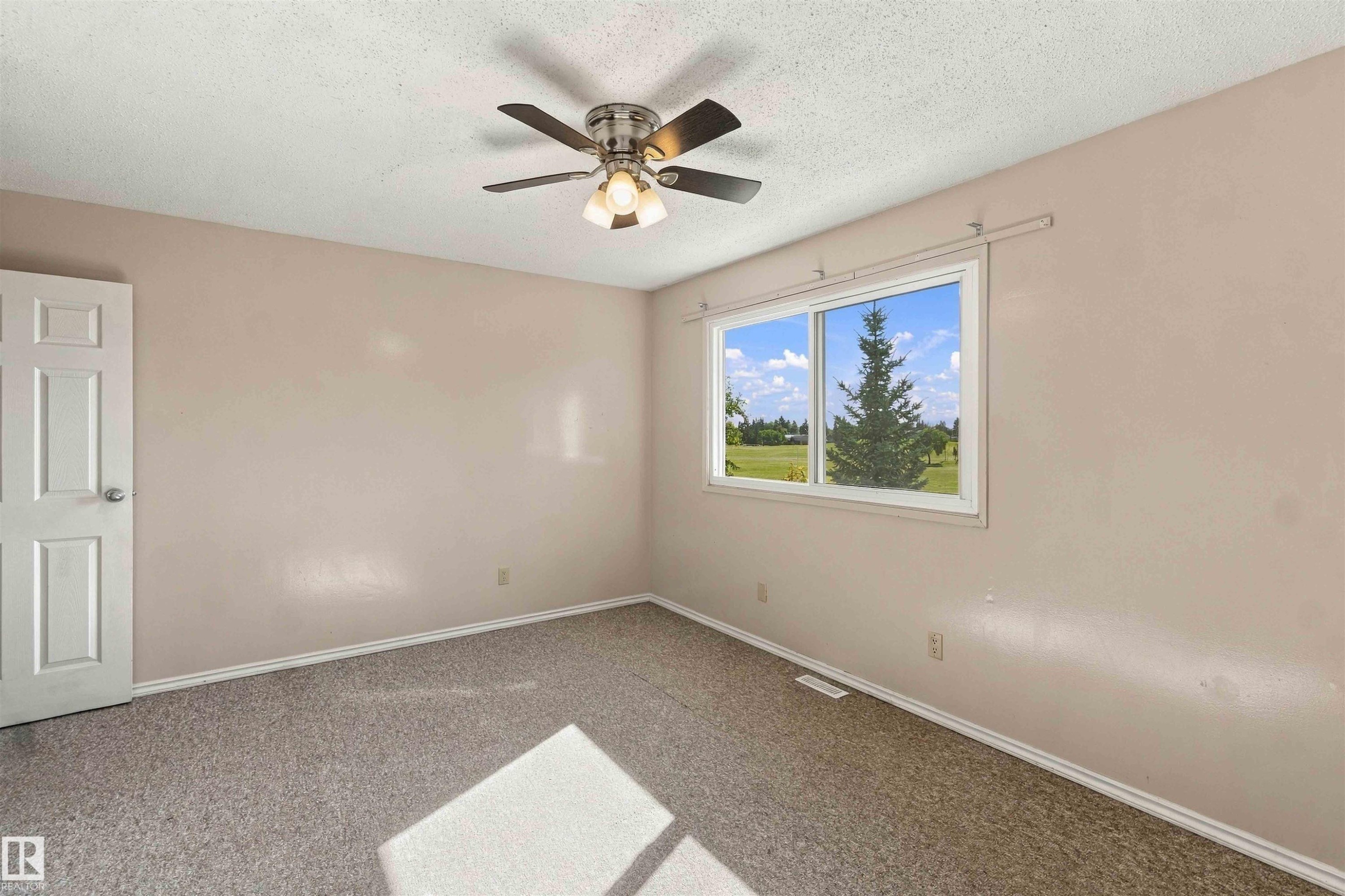 Neutral wall paint with textured carpeting, a ceiling fan with integrated lighting, and a white framed window offering outdoor scenery - 17351 85 Avenue Nw, Edmonton, AB