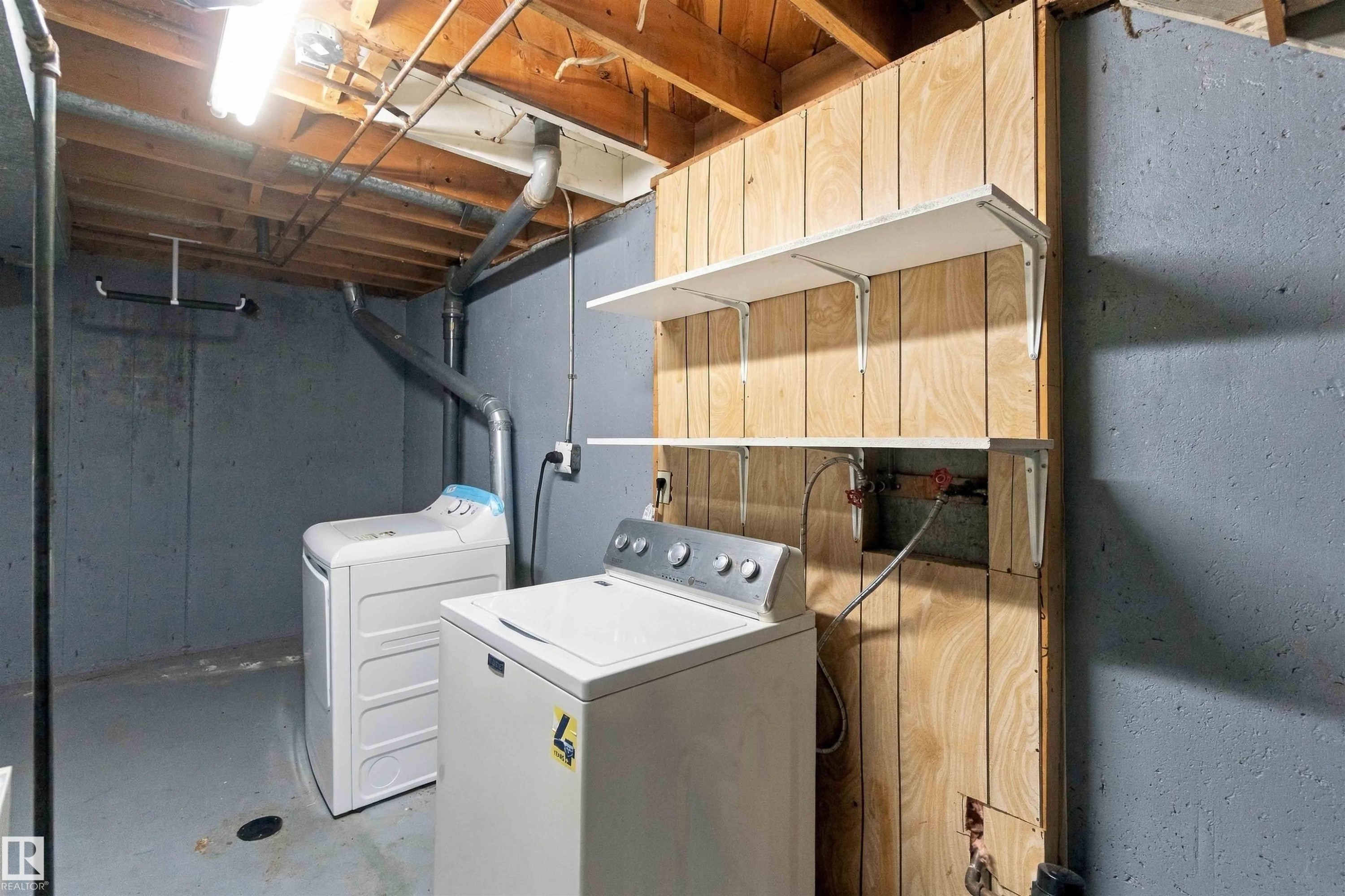 Laundry area featuring concrete walls, exposed wood ceiling joists, and built-in shelving - 17351 85 Avenue Nw, Edmonton, AB