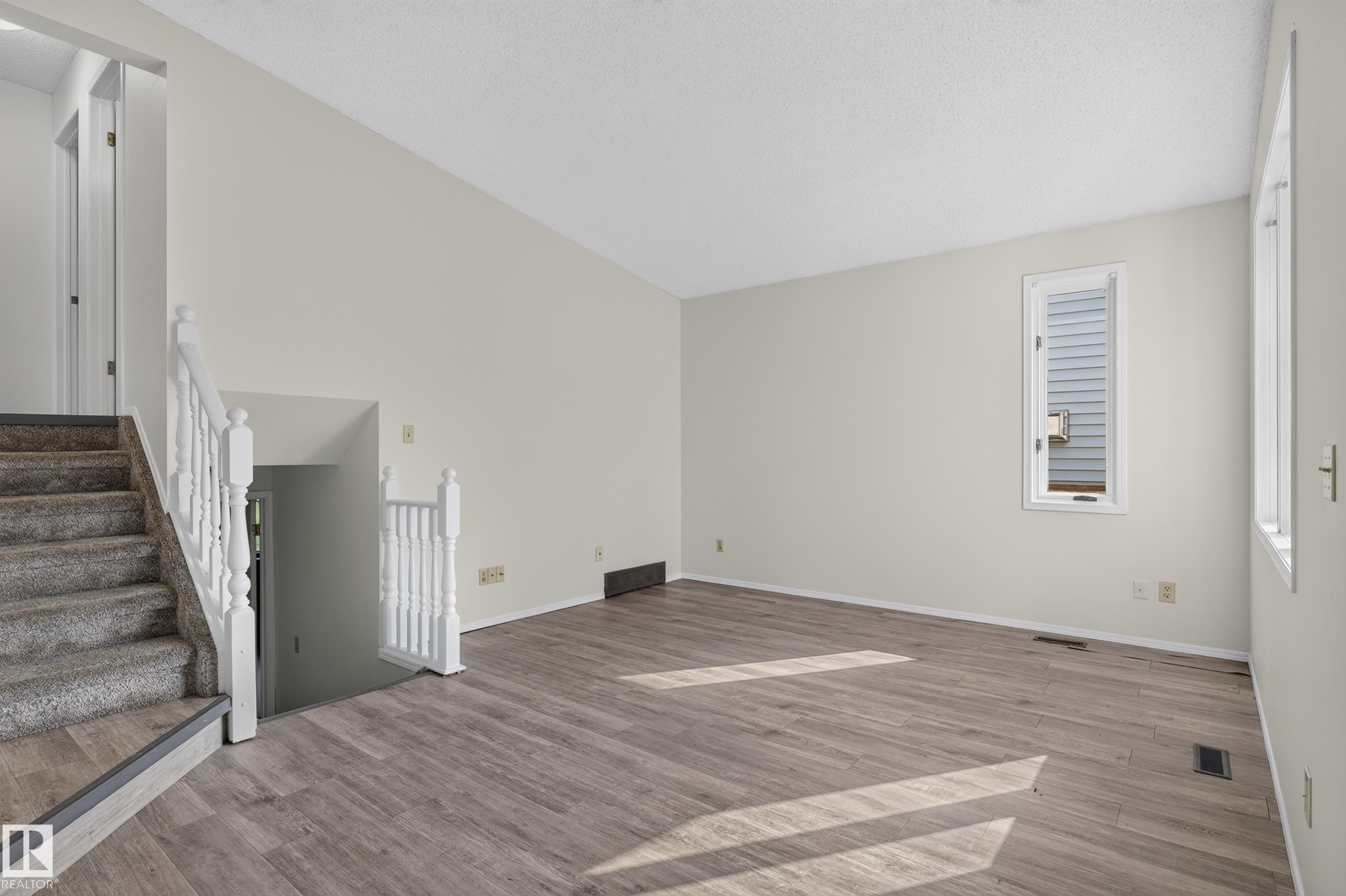 Vaulted ceiling, wood-finish flooring, white painted walls, white banister, and carpeted stairs - 3722 34A Avenue Nw, Edmonton, AB