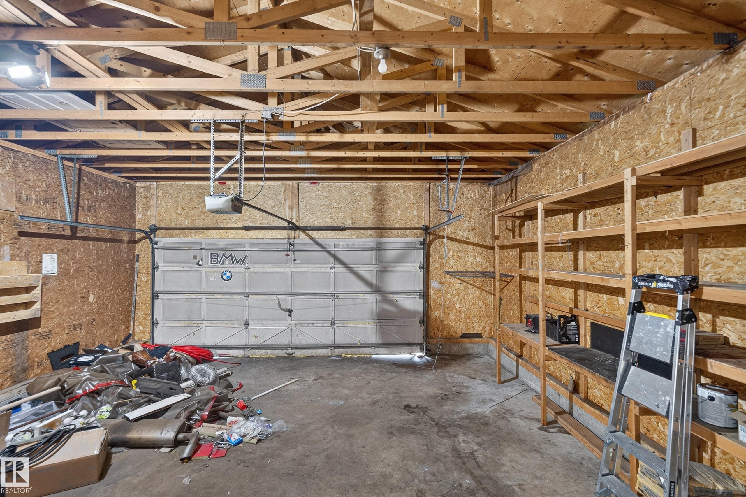 Garage space featuring exposed wood trusses, an automatic garage door opener, wood-finish walls, concrete flooring, and built-in wood shelving - 3722 34A Avenue Nw, Edmonton, AB