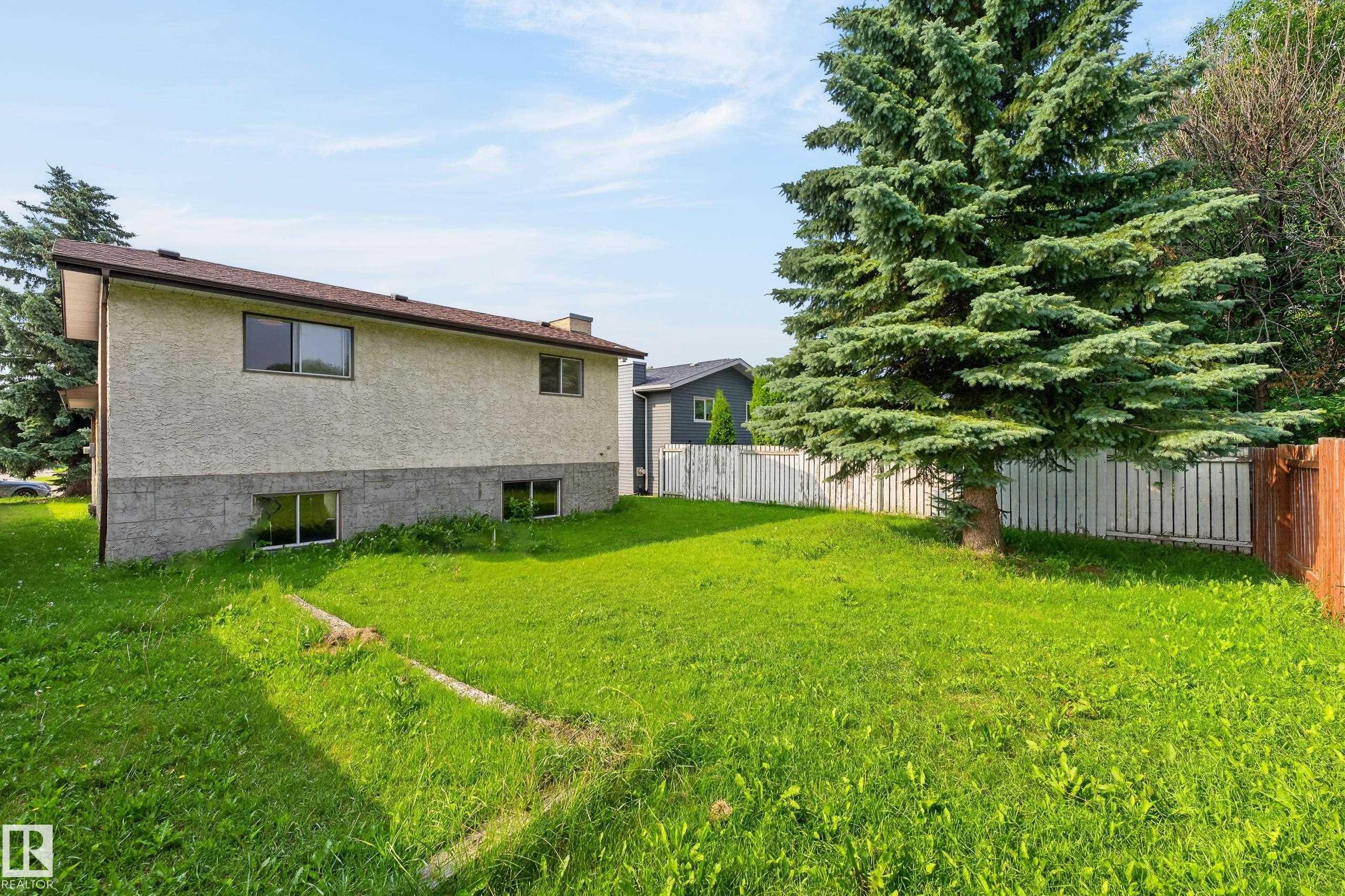 Stucco exterior with dark-framed windows, a prominent conifer, and a white picket fence - 3722 34A Avenue Nw, Edmonton, AB