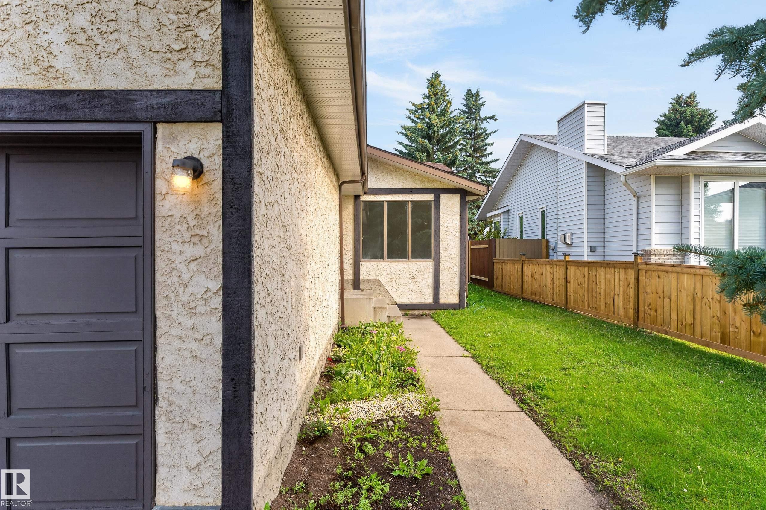 Stucco exterior with dark trim accents, attached garage with panel door, screened-in porch, concrete pathway, and a wooden fence - 3722 34A Avenue Nw, Edmonton, AB