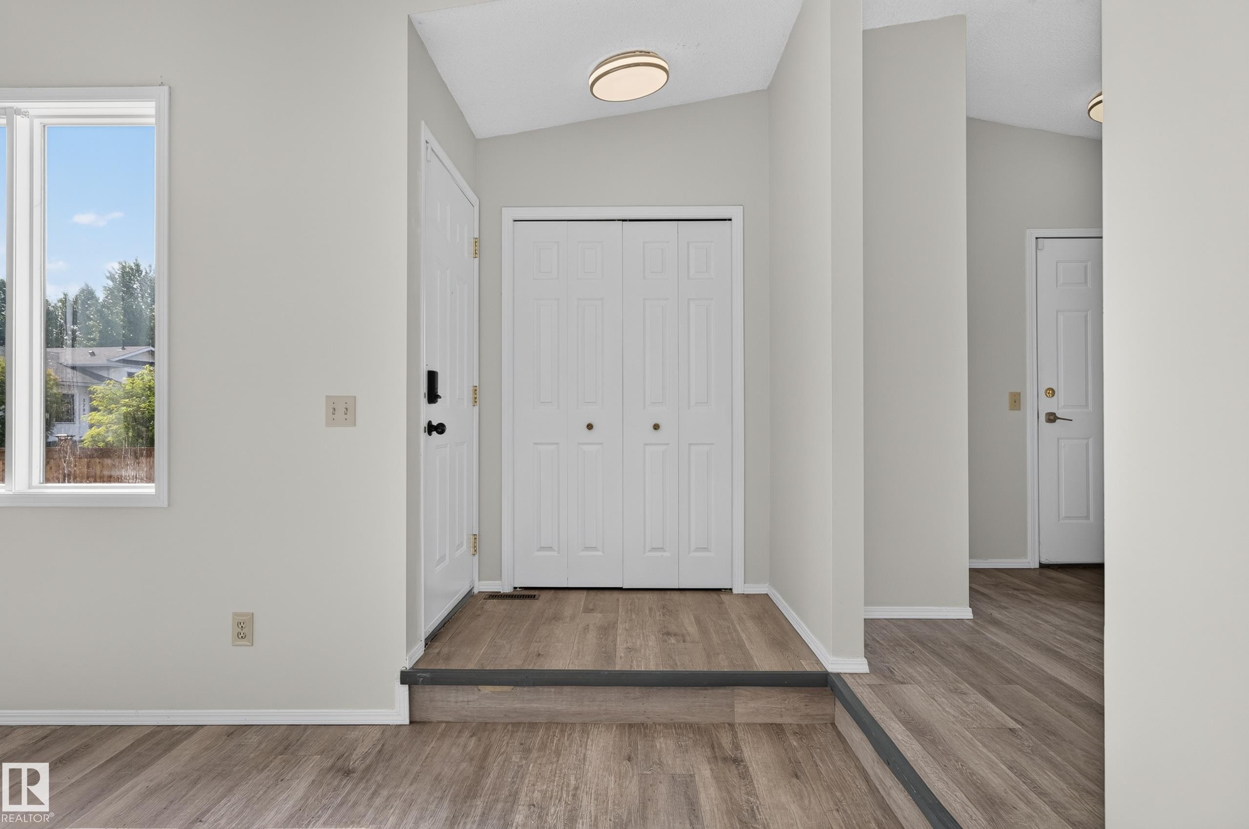 Entryway featuring wood-finish flooring, white paneled doors, and a contemporary flush-mount ceiling light - 3722 34A Avenue Nw, Edmonton, AB