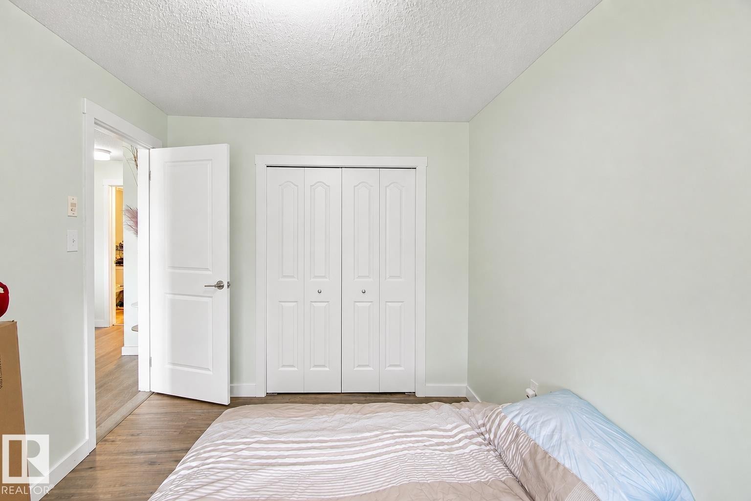 White bi-fold closet doors, white interior door, light-colored walls, wood-finish flooring - #413 18126 77 St Nw, Edmonton, AB
