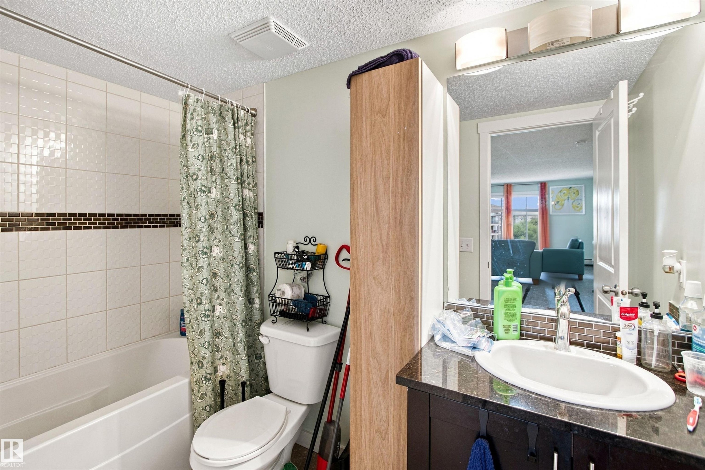 Bathtub with tiled surround, dark granite-finish countertop, and integrated vanity sink with a chrome faucet - #413 18126 77 St Nw, Edmonton, AB