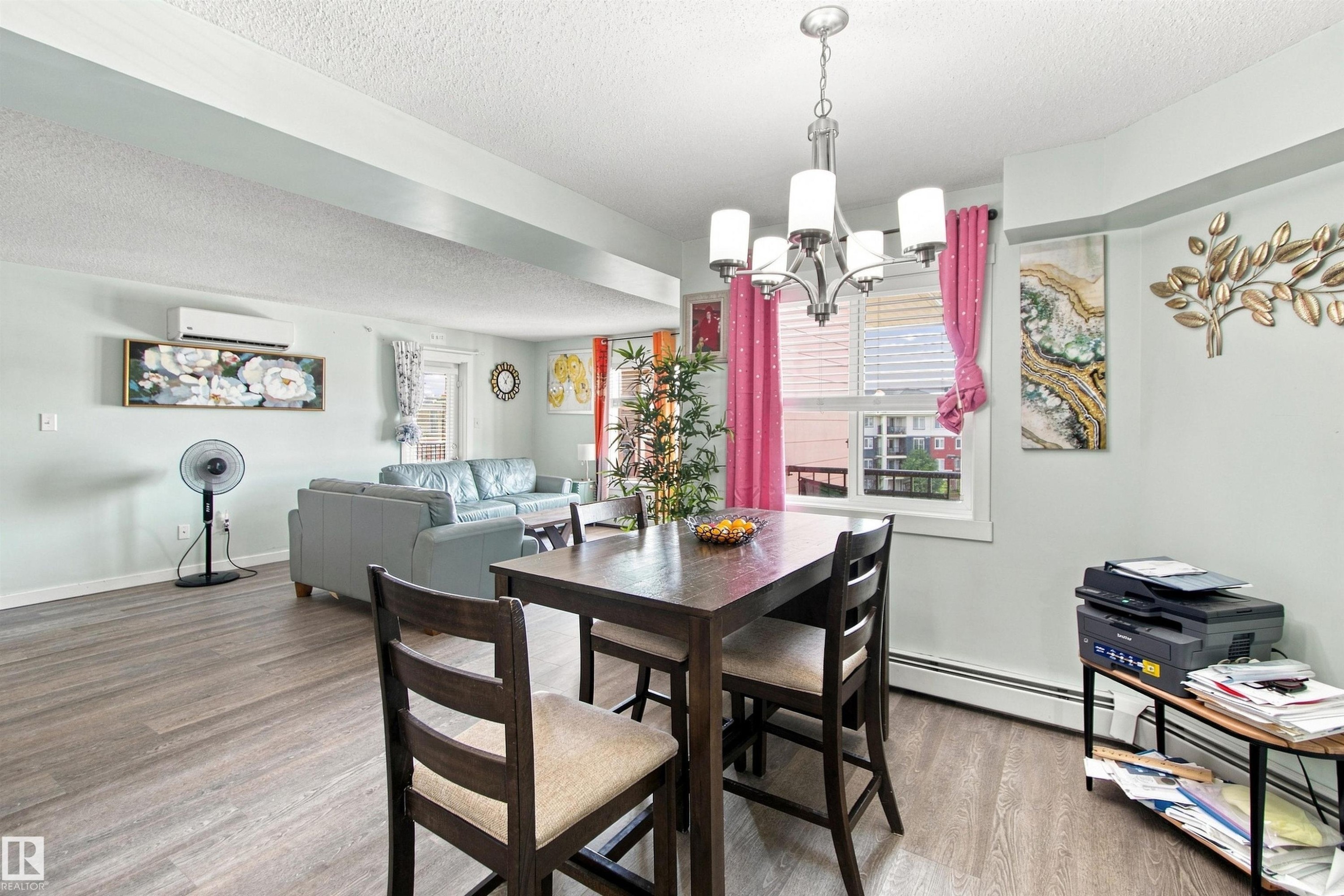 Open-concept living area featuring wood-finish flooring, a window with blinds, and a modern chandelier - #413 18126 77 St Nw, Edmonton, AB