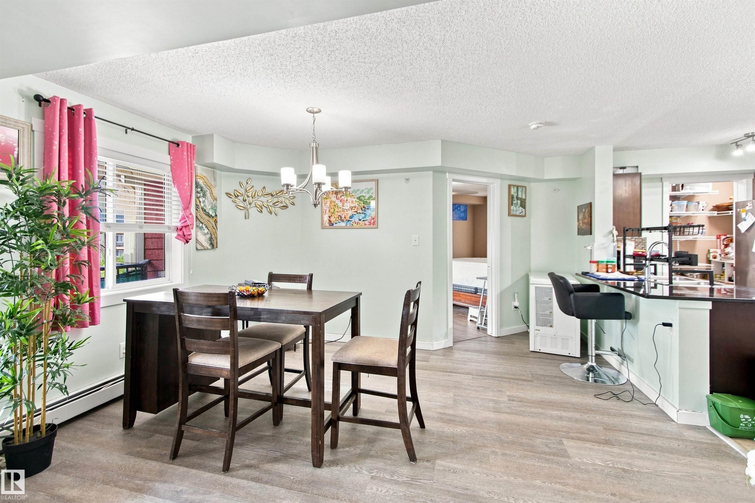 Wood-finish flooring, recessed lighting, and a modern chandelier illuminate the dining area and kitchen bar - #413 18126 77 St Nw, Edmonton, AB