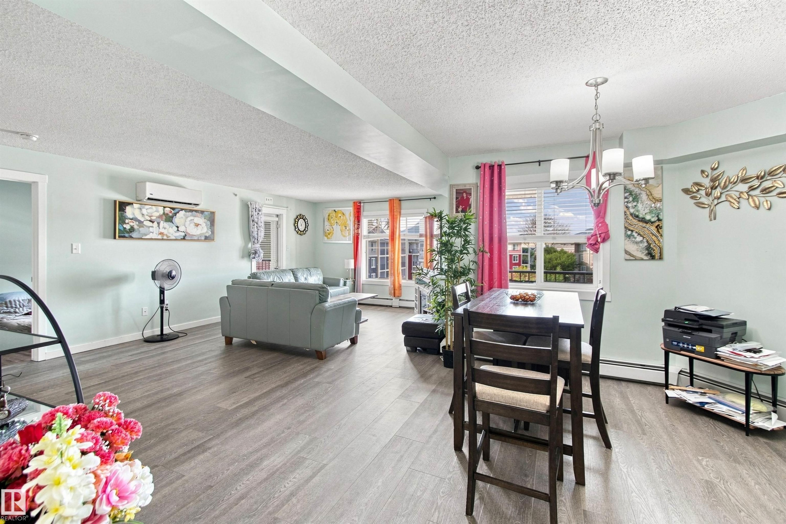 Open-concept living and dining area featuring wood-finish flooring, a wall-mounted climate control unit, and a suspended chandelier - #413 18126 77 St Nw, Edmonton, AB