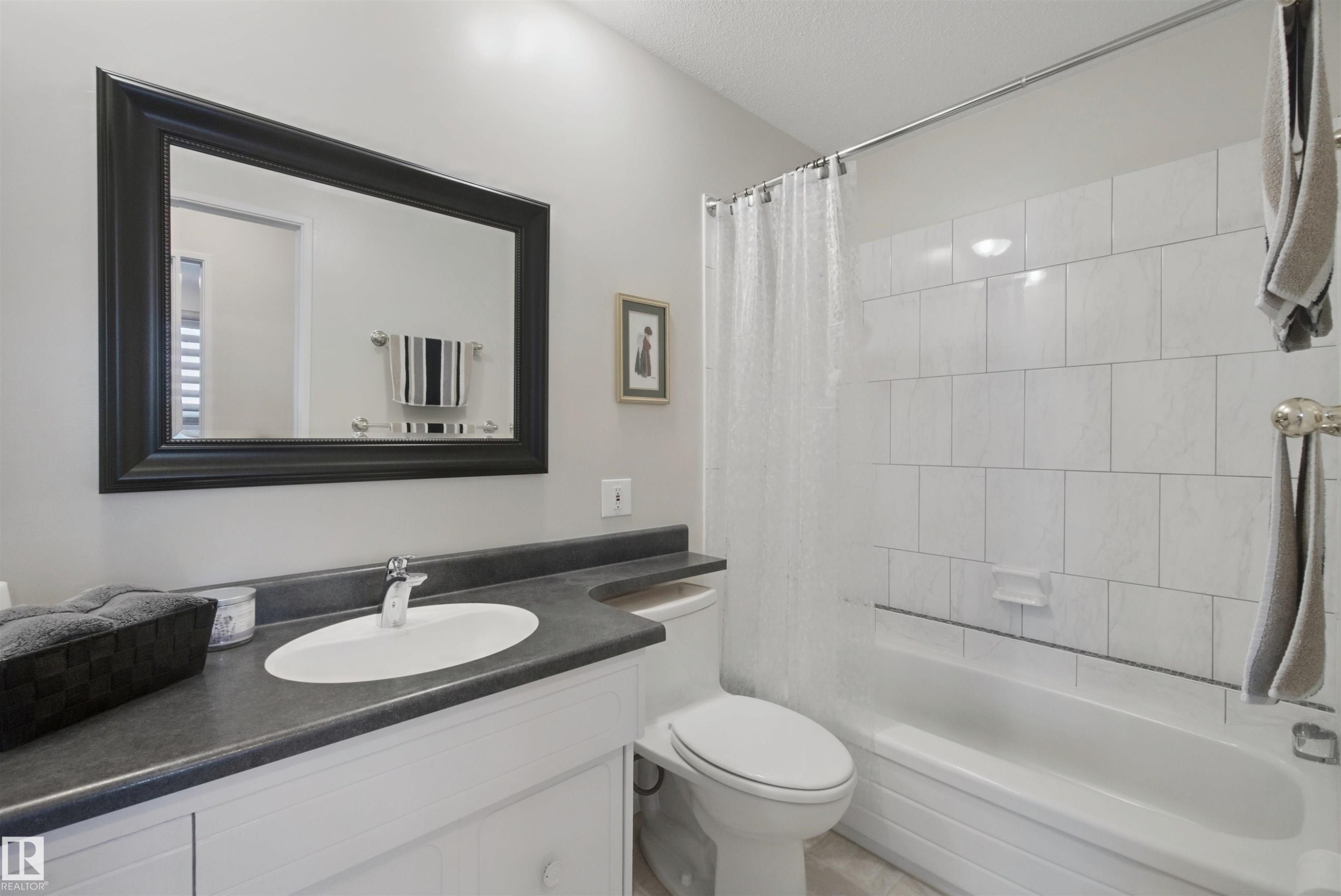White vanity with a dark countertop, an oval undermount sink, and a framed mirror - 11439 144 Avenue Nw, Edmonton, AB