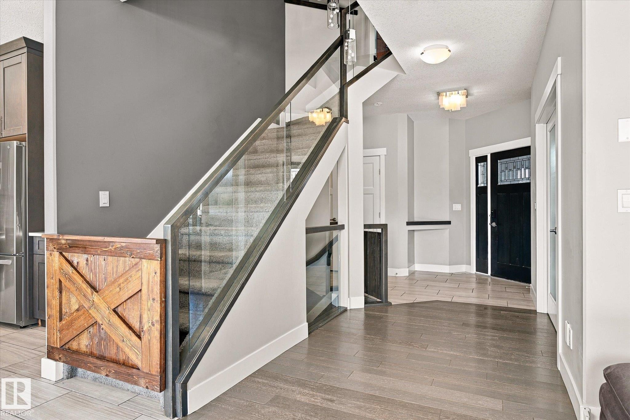 Modern staircase featuring glass railing and wood newel post - 2011 Genesis Lane, Stony Plain, AB