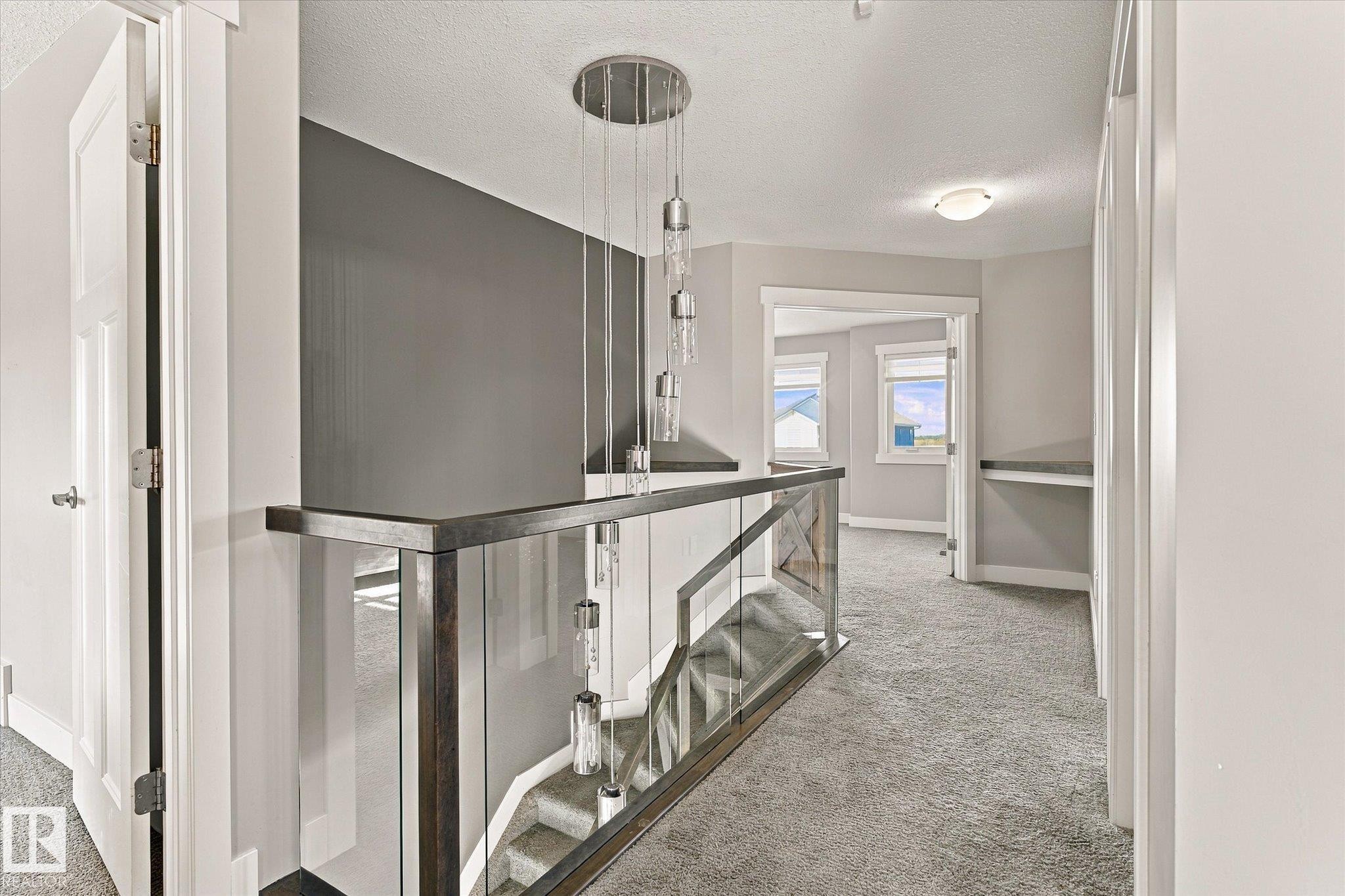 Modern chandelier, glass panel railing, wood-finish railing, carpeted flooring, and built-in desk - 2011 Genesis Lane, Stony Plain, AB