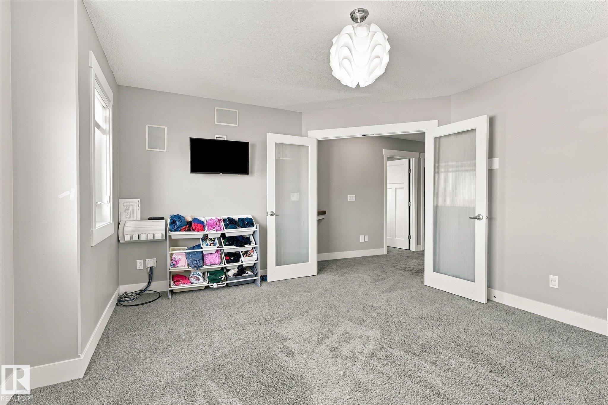 Plush carpet flooring, neutral wall tones, decorative ceiling light fixture, and French doors with frosted panels - 2011 Genesis Lane, Stony Plain, AB
