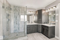 Walk-in shower with glass enclosure, dual vanity with undermount sinks, wood-finish flooring, and integrated cabinetry - 