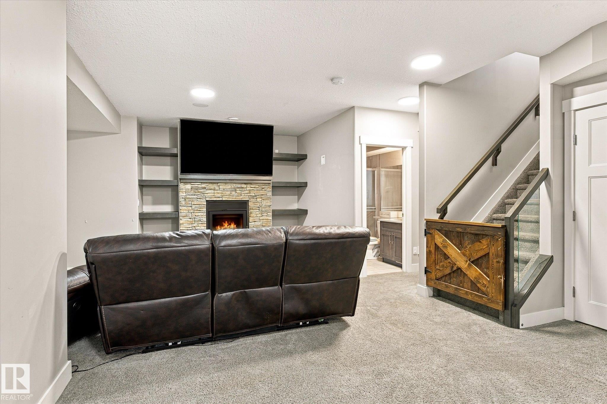 Stone fireplace with hearth, built-in shelving, recessed lighting, carpet flooring, and a staircase with glass panel railing - 2011 Genesis Lane, Stony Plain, AB