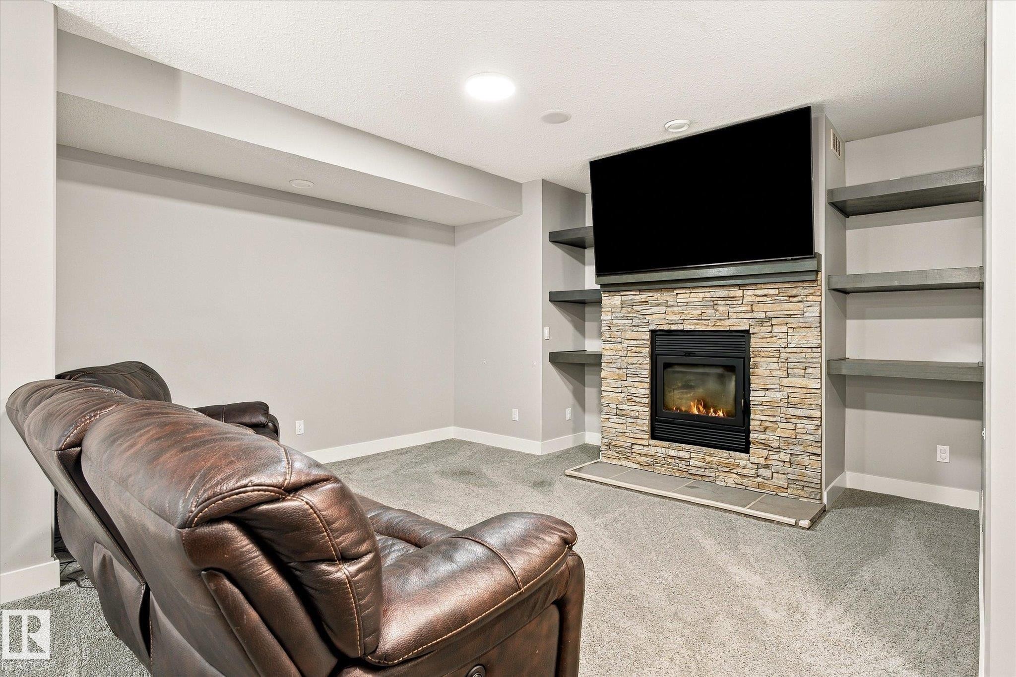 Recessed lighting, built-in shelving, stone-faced fireplace with hearth, and carpeted flooring - 2011 Genesis Lane, Stony Plain, AB