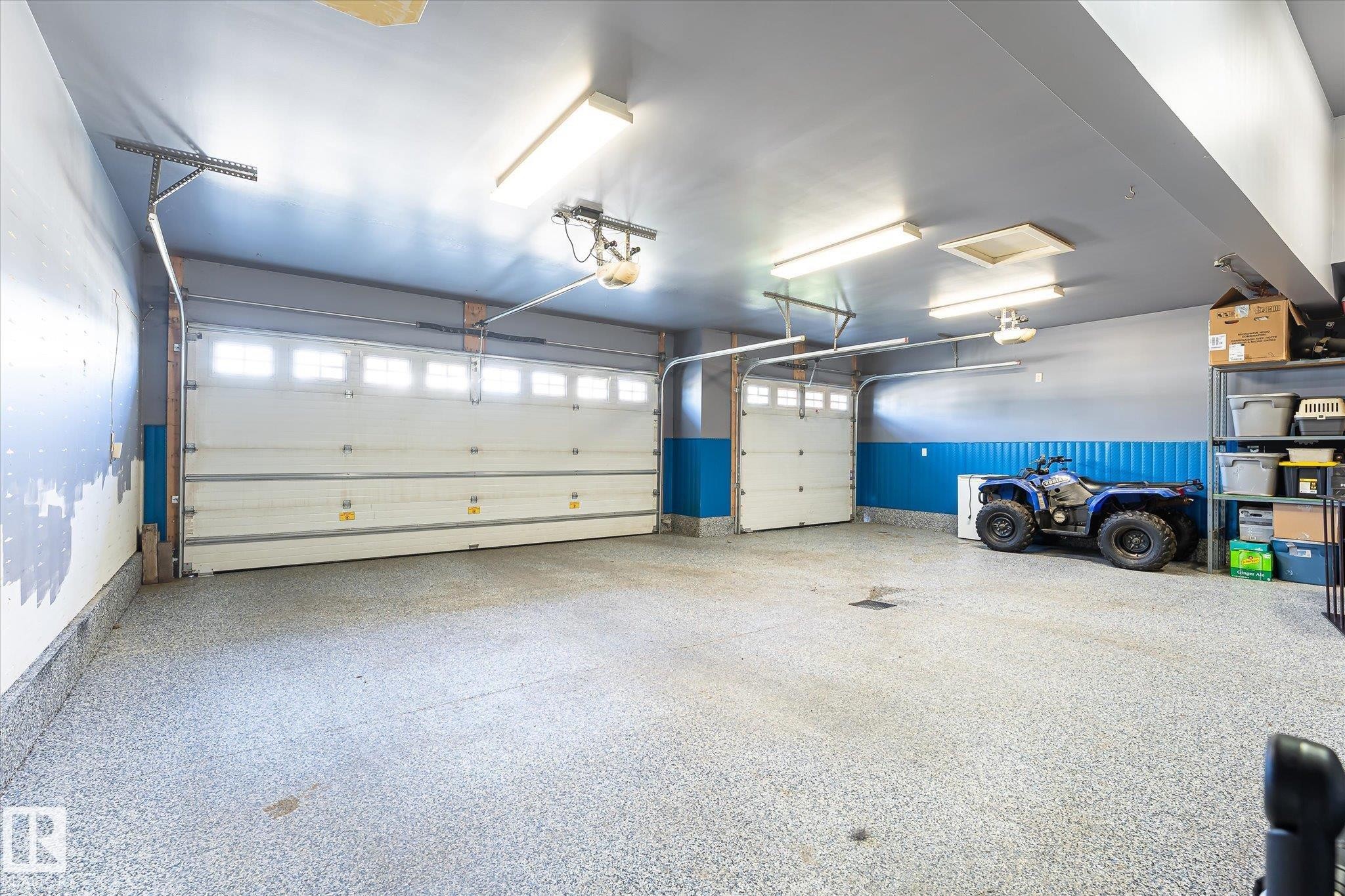 Multi-car garage featuring two overhead garage doors, overhead lighting, and a textured floor finish - 2011 Genesis Lane, Stony Plain, AB