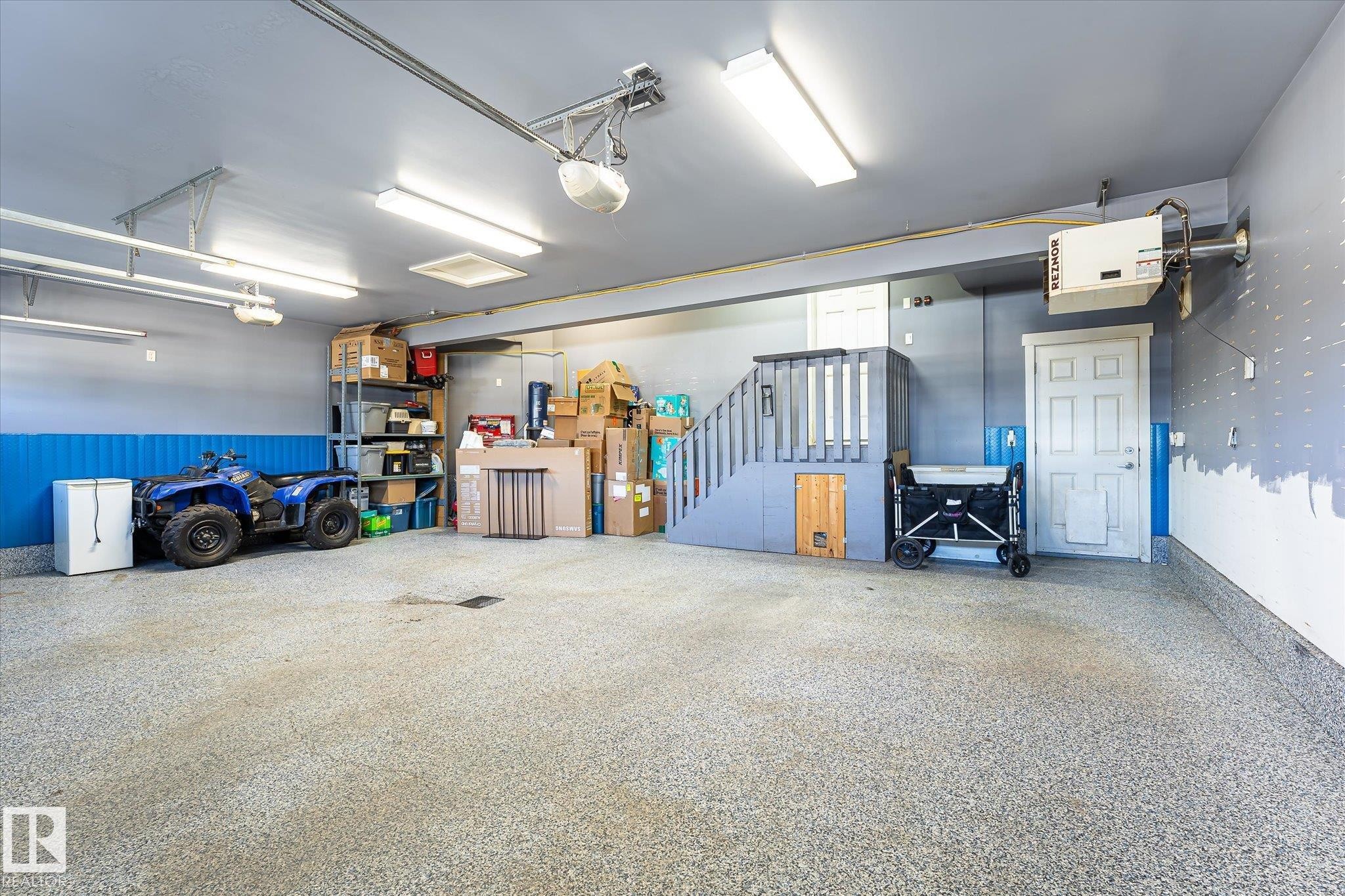 Spacious garage with an epoxy-coated floor, overhead fluorescent lighting, and built-in staircase with integrated storage - 2011 Genesis Lane, Stony Plain, AB