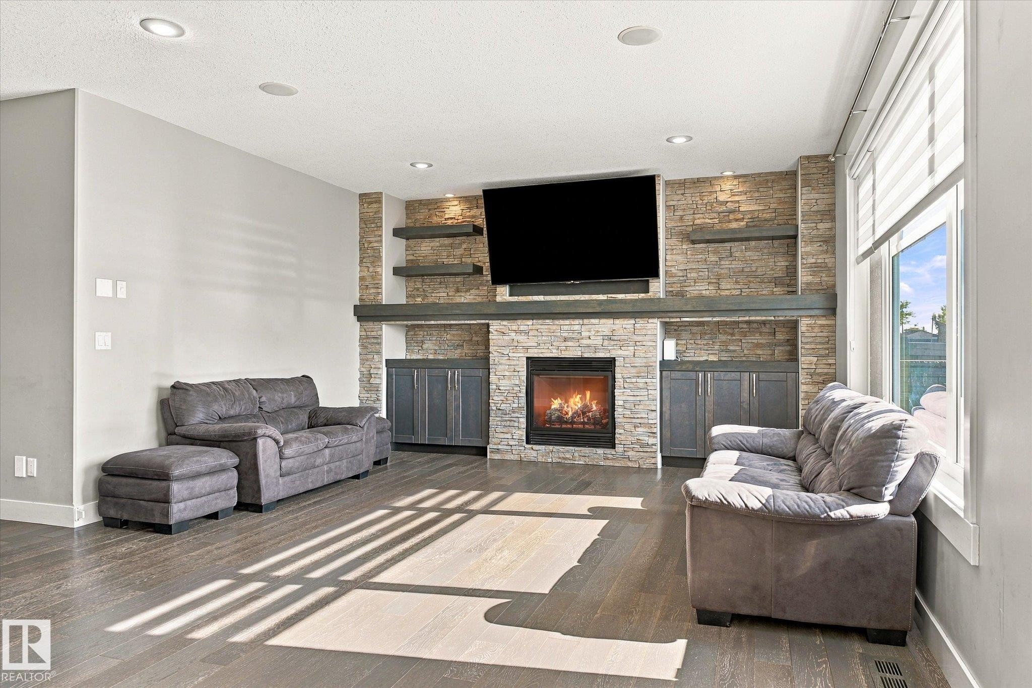 Stone-clad fireplace with built-in cabinetry, wood-finish flooring, recessed lighting, and large windows with blinds - 2011 Genesis Lane, Stony Plain, AB