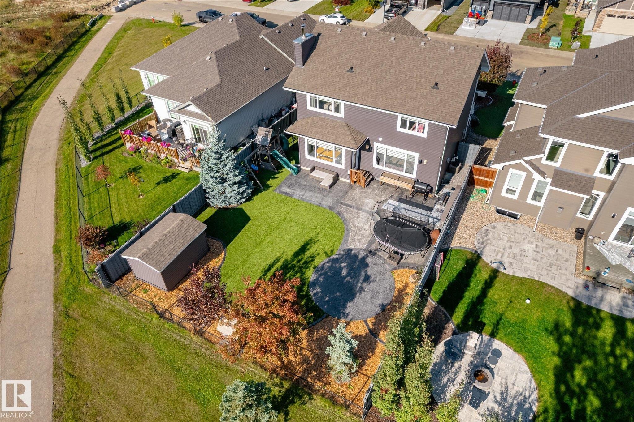 Expansive backyard featuring a manicured lawn, multiple paver patio areas, mature trees, and a storage shed - 2011 Genesis Lane, Stony Plain, AB