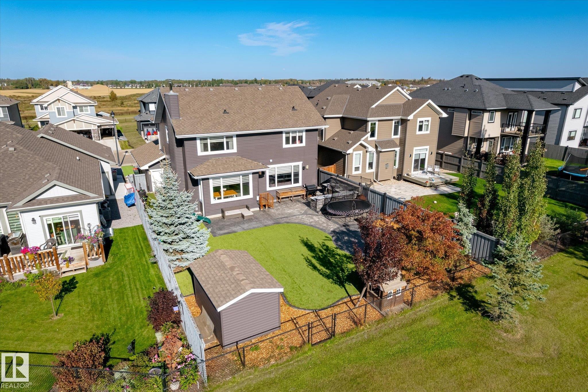 Expansive backyard featuring a manicured lawn, a large paver patio, a utility shed, and mature landscaping - 2011 Genesis Lane, Stony Plain, AB