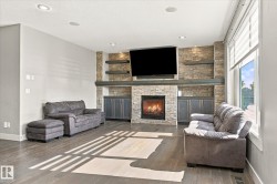 Stone-clad fireplace with built-in cabinetry, wood-finish flooring, recessed lighting, and large windows with blinds - 