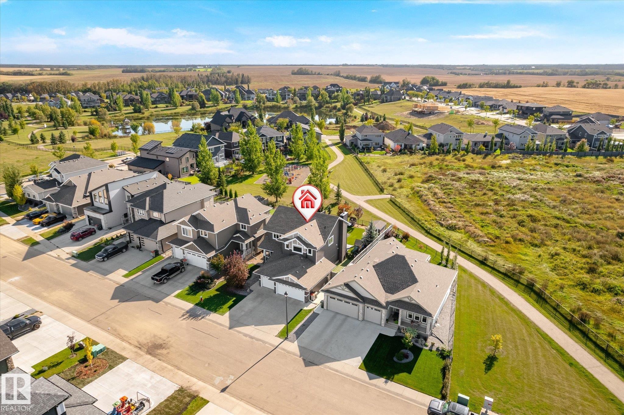 Aerial perspective showcasing a residential neighborhood with landscaped properties, a street, and a nearby pond - 2011 Genesis Lane, Stony Plain, AB