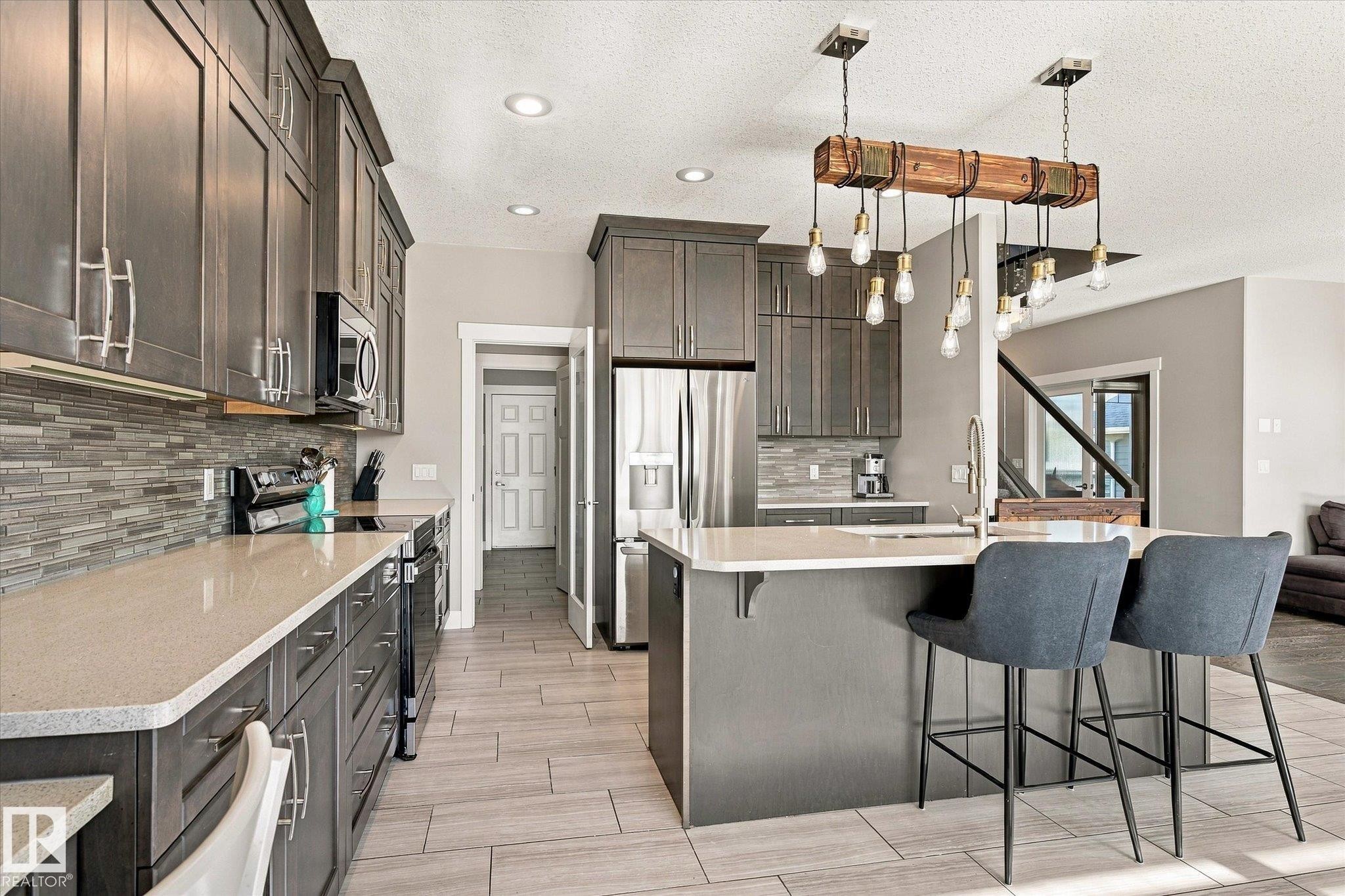 Kitchen featuring dark wood-finish cabinetry, light-toned countertops, a mosaic tile backsplash, and stainless steel appliances - 2011 Genesis Lane, Stony Plain, AB