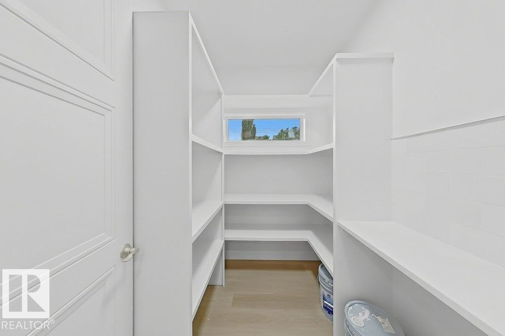 Walk-in pantry featuring white shelving, a transom window, and wood-finish flooring - 9216 91 Street Nw, Edmonton, AB - Indoor
