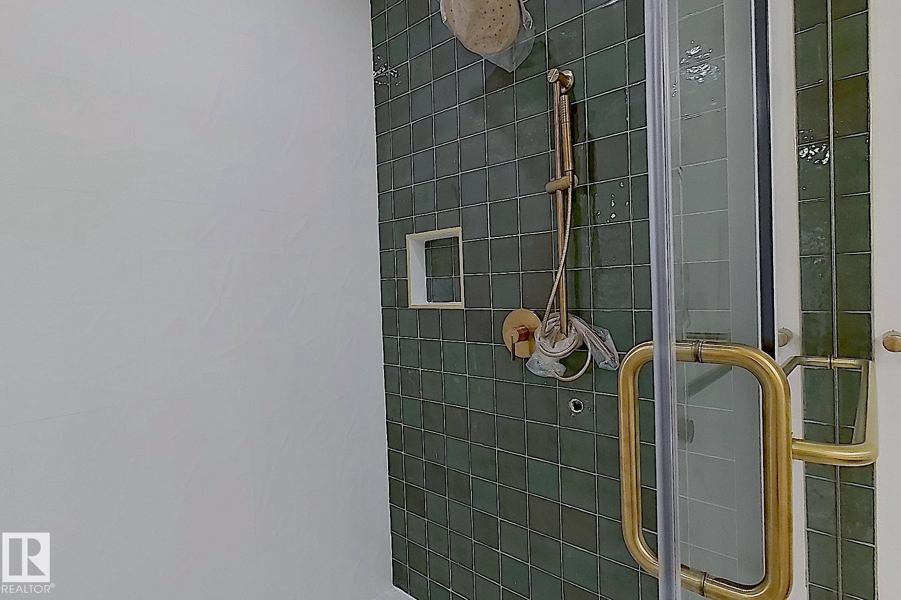 Shower enclosure featuring green square tile, gold-finish shower fixtures, a built-in shower niche, and a clear glass door with a gold-finish handle - 9216 91 Street Nw, Edmonton, AB -