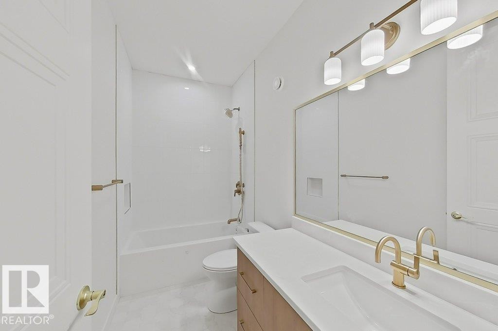 Bathroom featuring a neutral color palette, integrated sink vanity with a wood-finish base, wall-mounted mirror with brass trim, and a bathtub with white subway tile surround and brass fixtures - 9216 91 Street Nw, Edmonton, AB - Indoor Photo Showing Other Room
