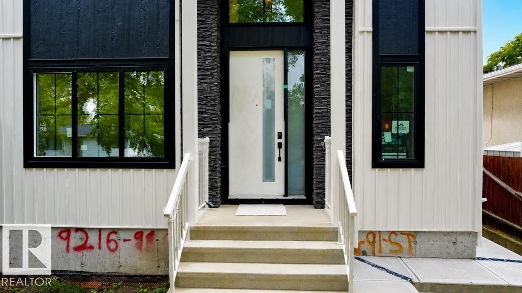 Contemporary exterior featuring vertical white siding, dark stacked stone accents, a modern entry door with sidelight, and black-framed windows - 9216 91 Street Nw, Edmonton, AB - Outdoor With Exterior