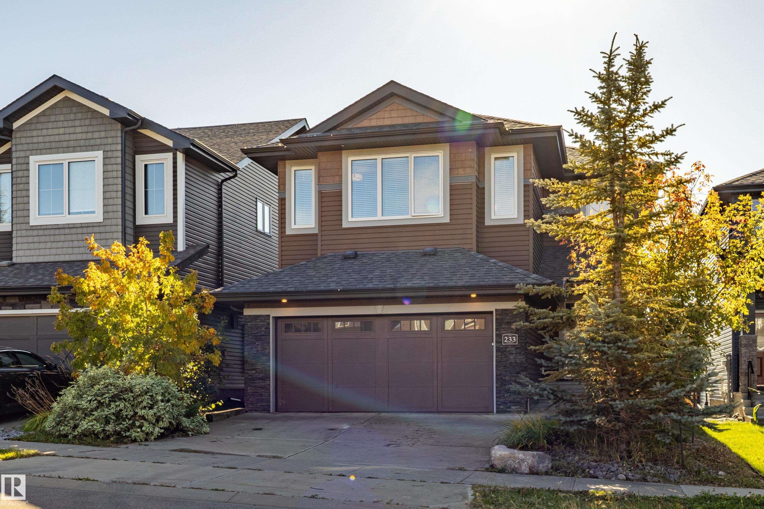 Two-story property featuring a double-bay garage, stone facade accents, multi-pane windows, and a shingled roof - 233 Hawks Ridge Boulevard Nw, Edmonton, AB