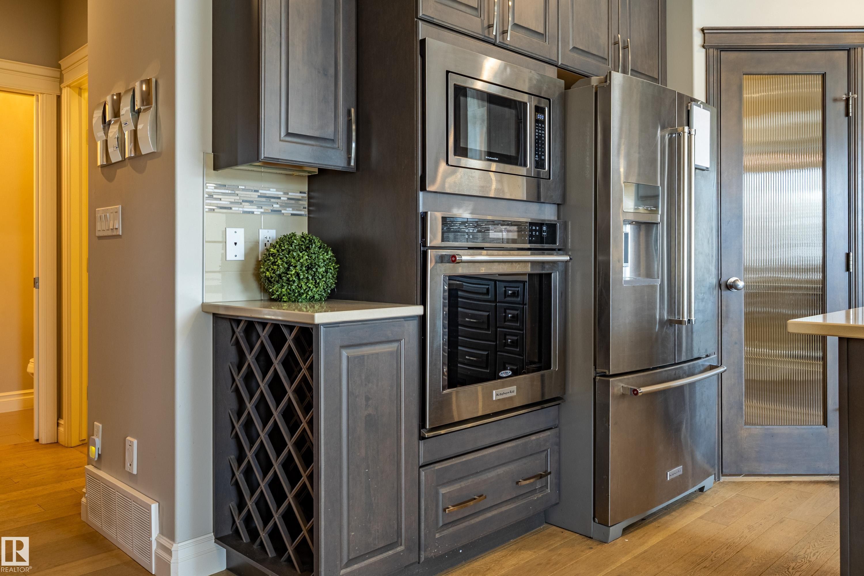 Built-in stainless steel appliances, custom cabinetry, integrated wine storage, wood-finish flooring, and a decorative frosted glass paneled door - 233 Hawks Ridge Boulevard Nw, Edmonton, AB