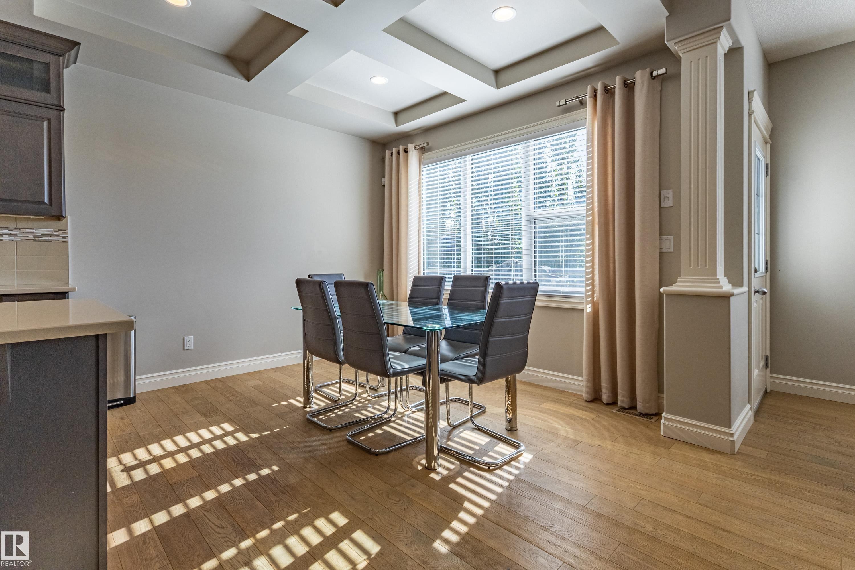 Recessed lighting, tray ceiling details, wood-finish flooring, a large window with blinds, and decorative column accents - 233 Hawks Ridge Boulevard Nw, Edmonton, AB