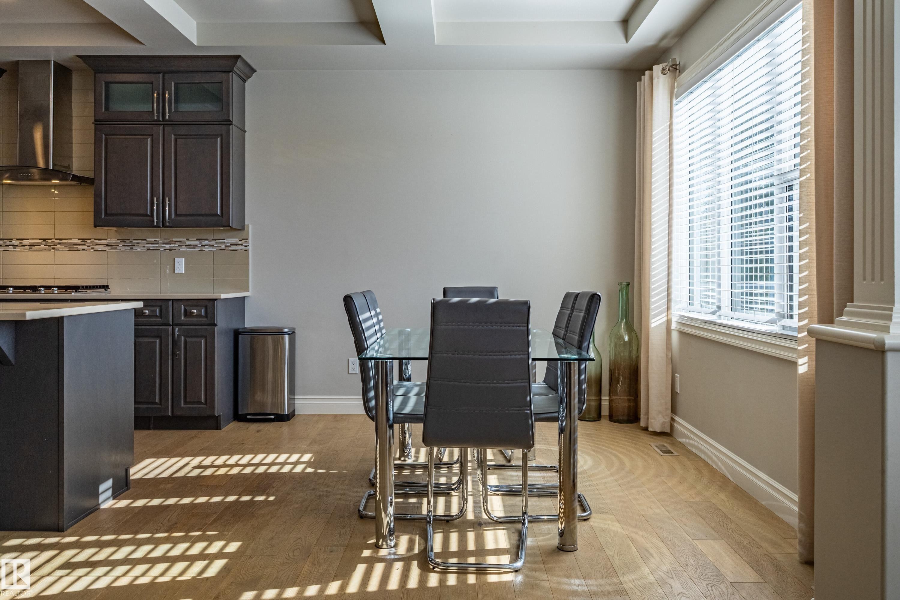 Kitchen and dining area featuring wood-finish flooring, dark wood cabinetry, a tiled backsplash, and a large window with blinds - 233 Hawks Ridge Boulevard Nw, Edmonton, AB