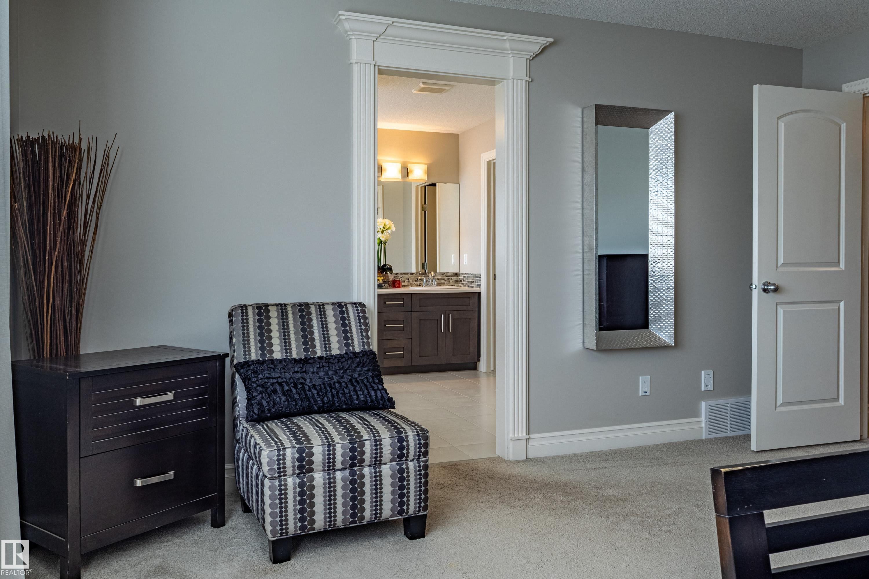 Cased doorway with decorative trim, leading to a bathroom featuring a vanity with dual sinks, wall-mounted light fixtures, and a framed mirror - 233 Hawks Ridge Boulevard Nw, Edmonton, AB