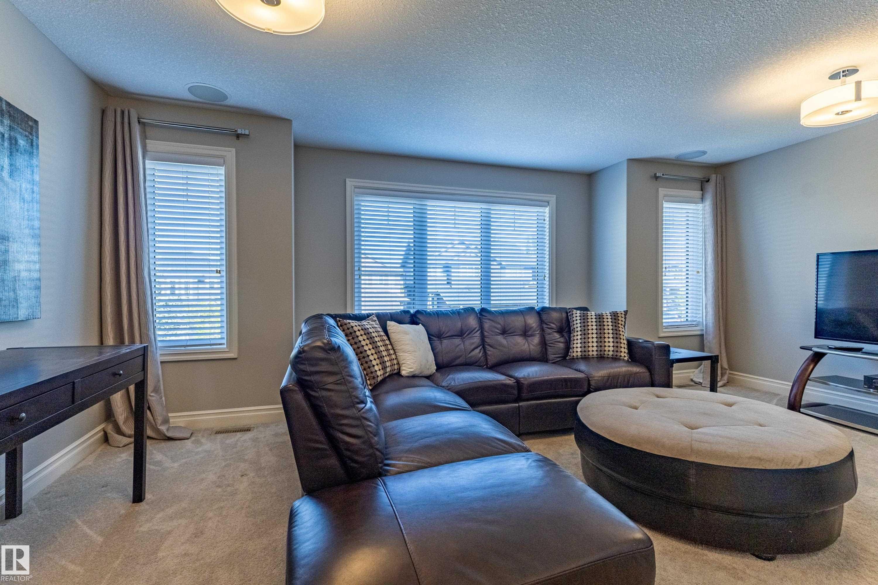 Carpeted living area with multiple windows, recessed ceiling speaker, and flush mount lighting fixtures - 233 Hawks Ridge Boulevard Nw, Edmonton, AB