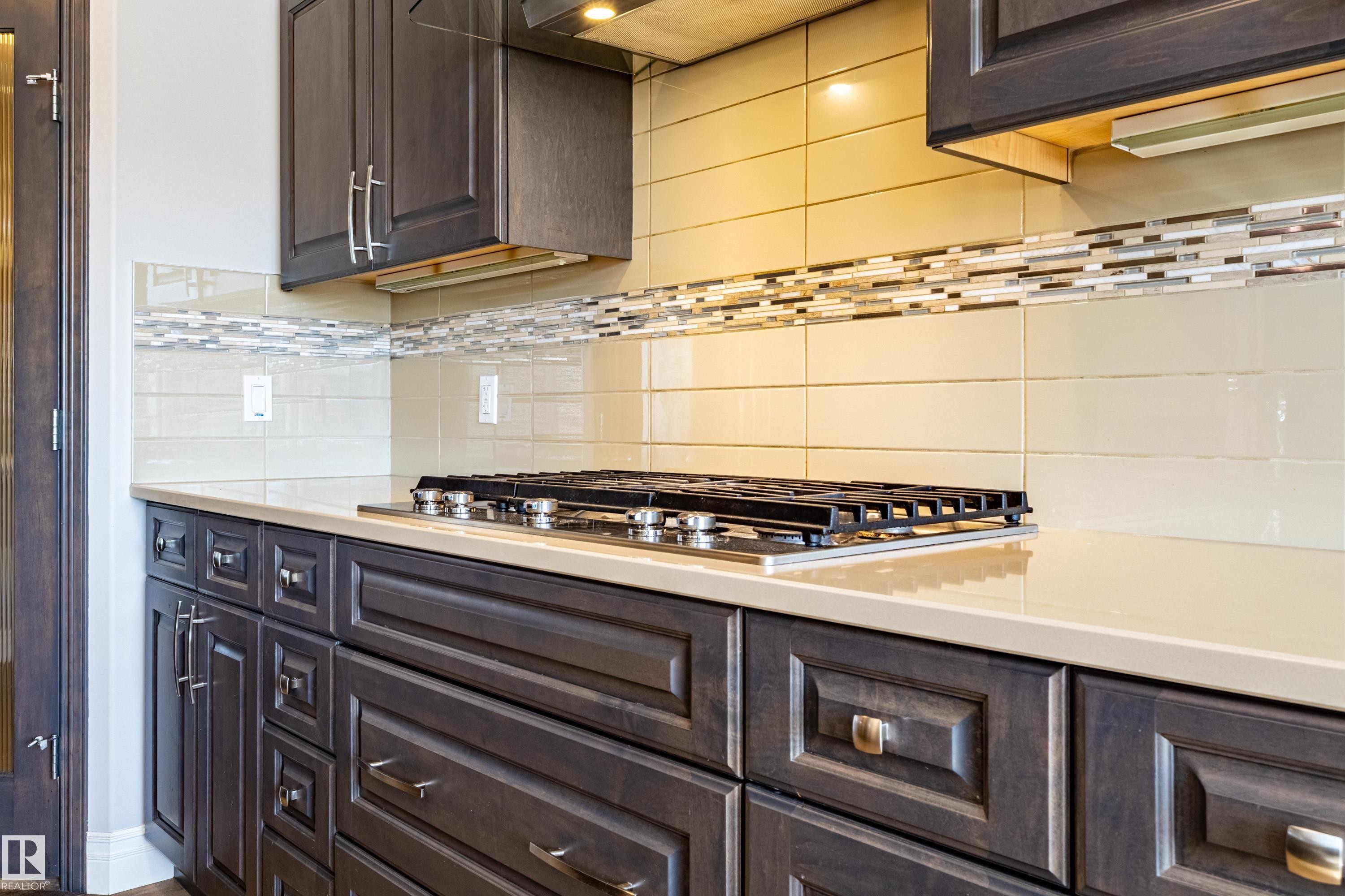 Built-in gas cooktop, light-toned countertop, and dark wood-finish cabinetry - 233 Hawks Ridge Boulevard Nw, Edmonton, AB