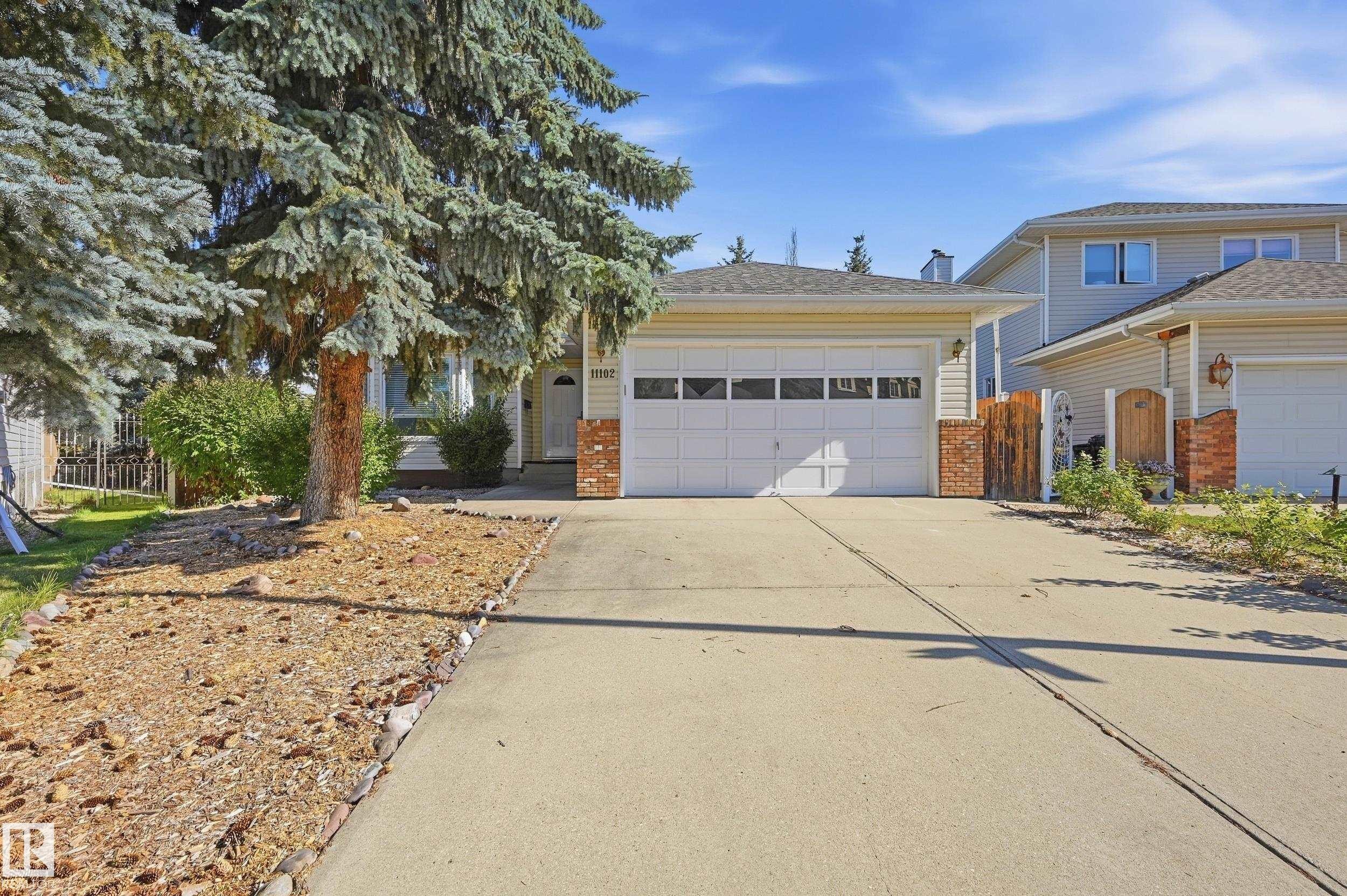 Light-colored siding exterior with brick accents, an attached two-car garage, and mature landscaping - 11102 11A Avenue Nw, Edmonton, AB