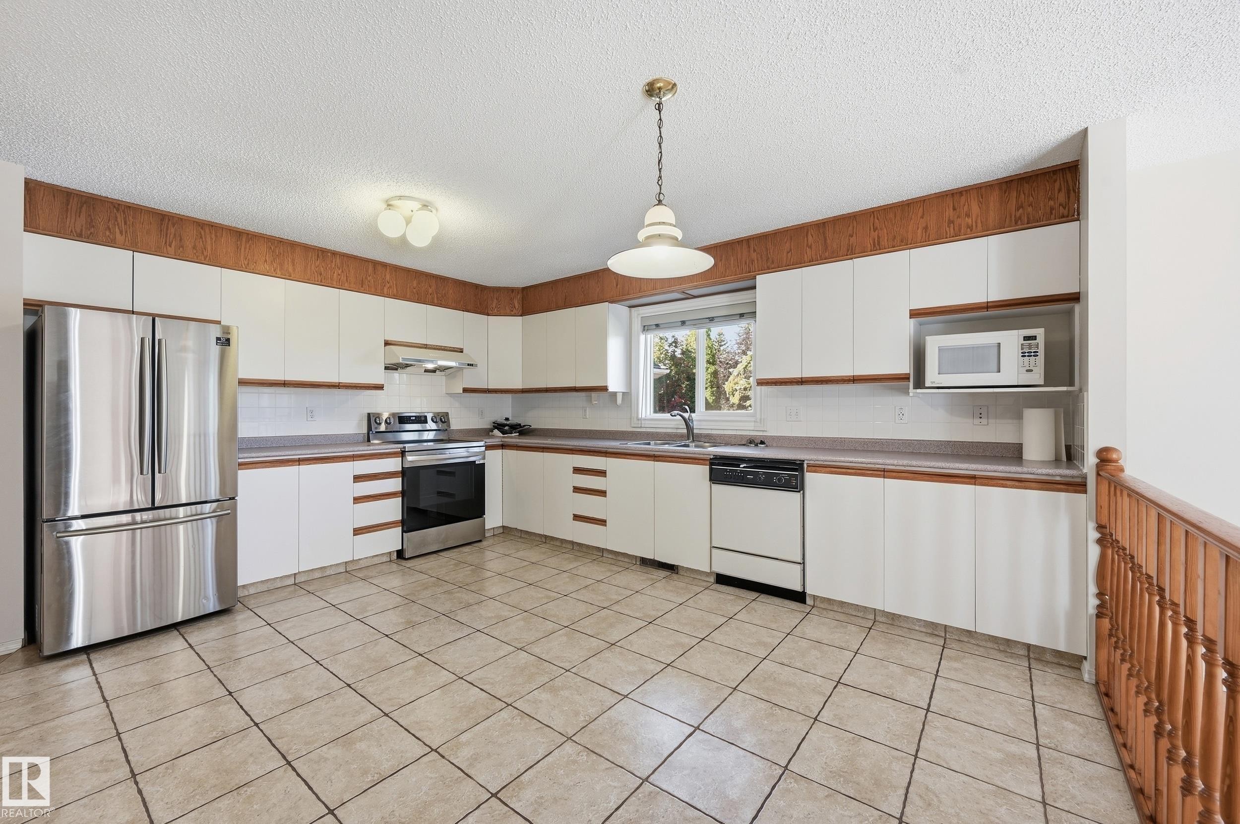 Spacious kitchen featuring tile flooring, white cabinetry with wood-finish accents, stainless steel appliances, and a built-in microwave - 11102 11A Avenue Nw, Edmonton, AB