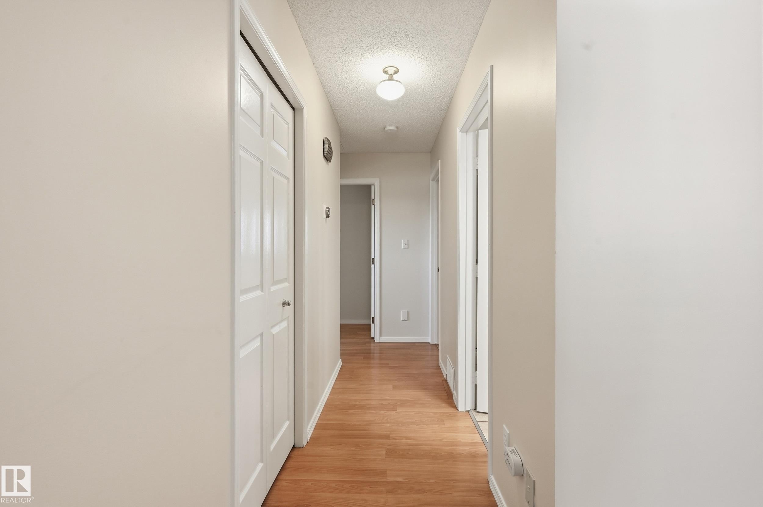 Wood-finish flooring throughout the hallway, featuring light-toned walls and multiple paneled doors - 11102 11A Avenue Nw, Edmonton, AB