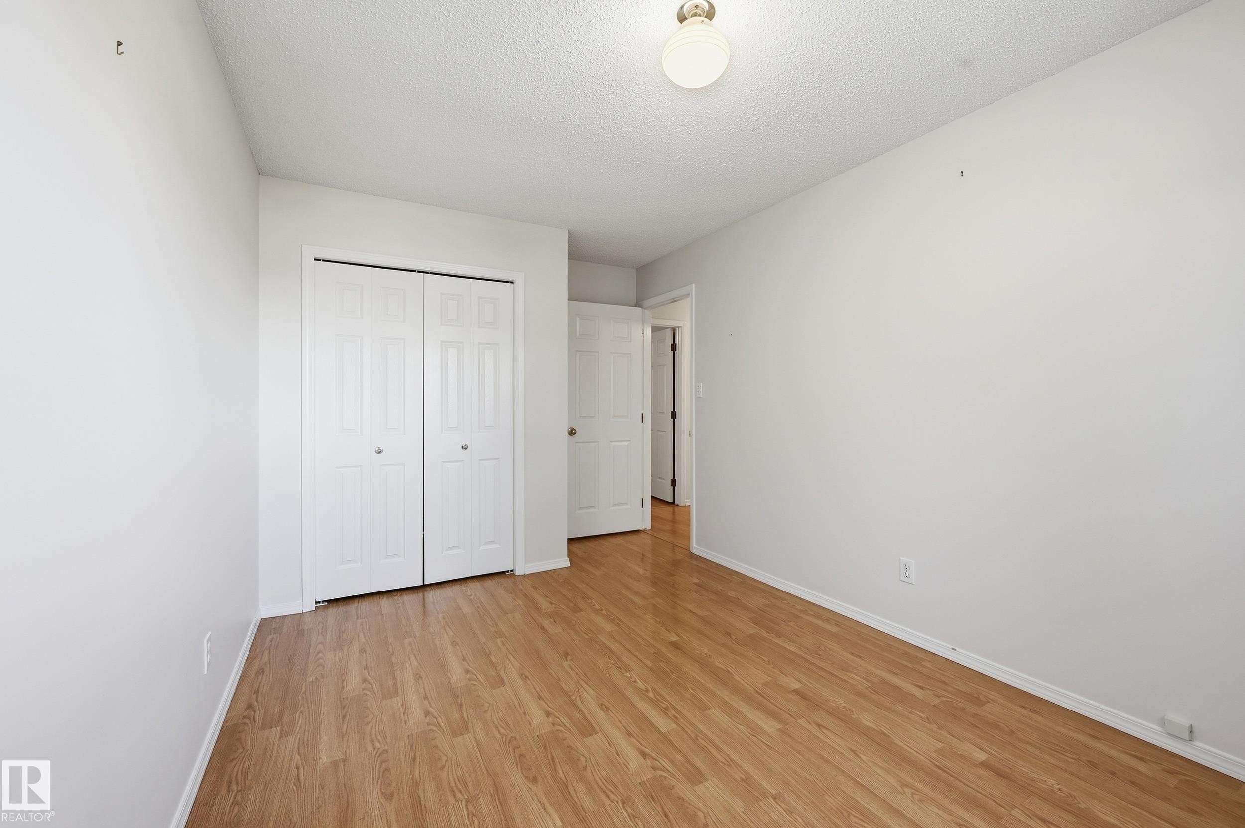 Wood-finish flooring with white walls, a built-in closet with bi-fold doors, and a ceiling-mounted light fixture - 11102 11A Avenue Nw, Edmonton, AB