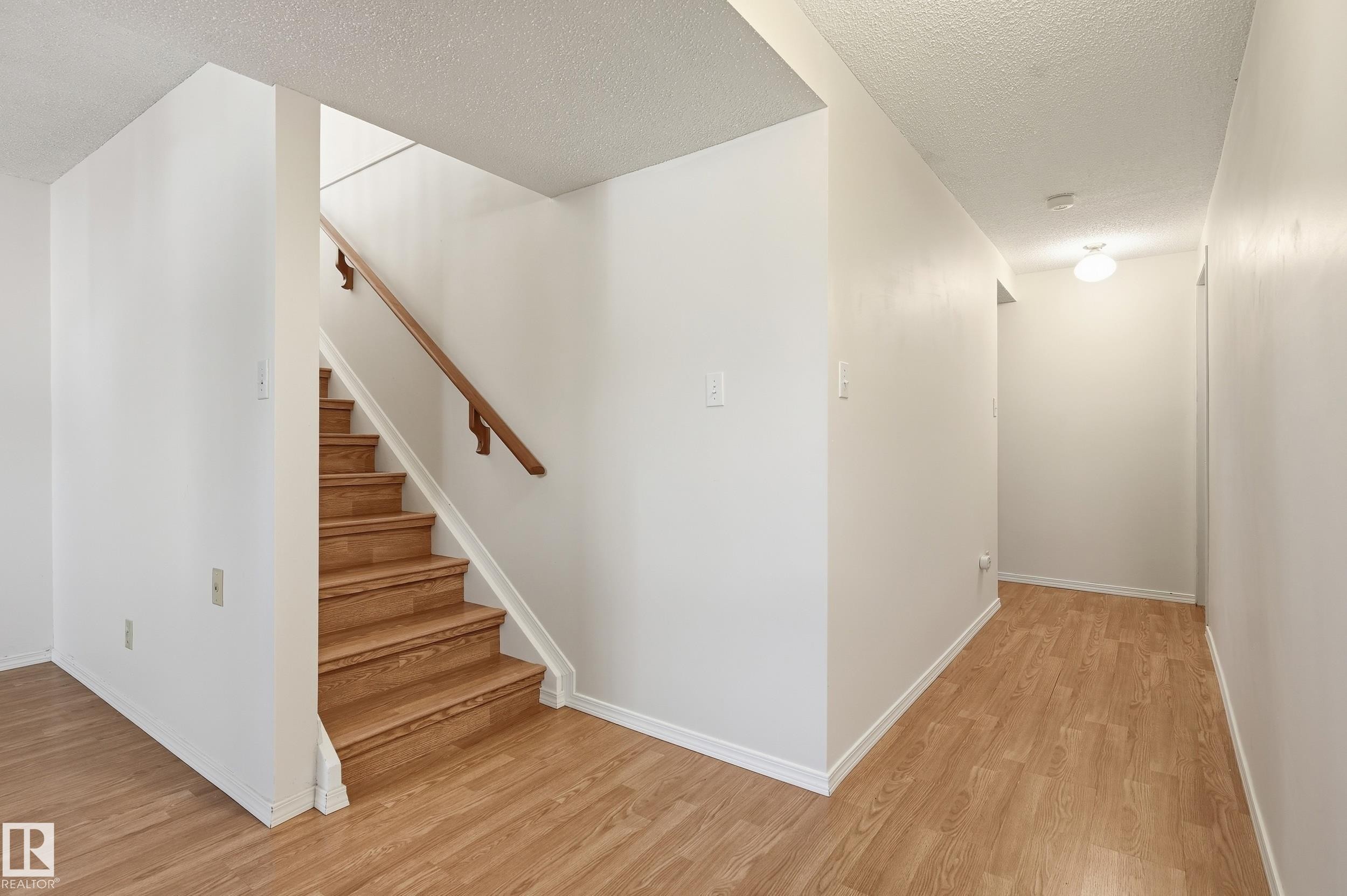 Wood-finish flooring throughout, white painted walls, and a staircase with a wood handrail - 11102 11A Avenue Nw, Edmonton, AB