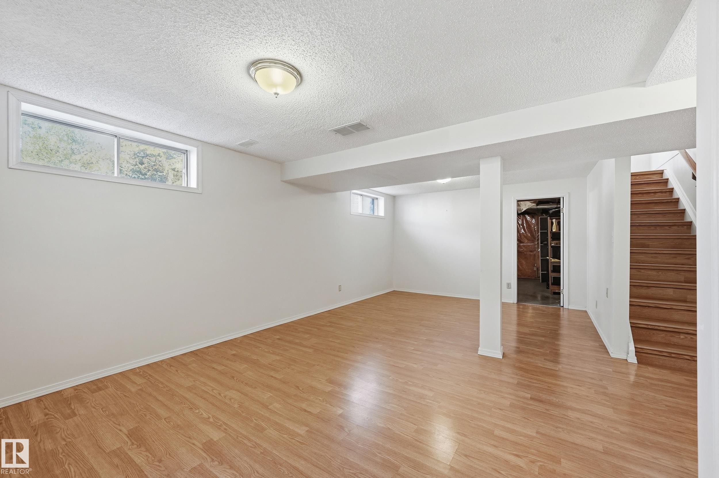 Spacious lower level featuring wood-finish flooring, recessed lighting, and multiple windows - 11102 11A Avenue Nw, Edmonton, AB